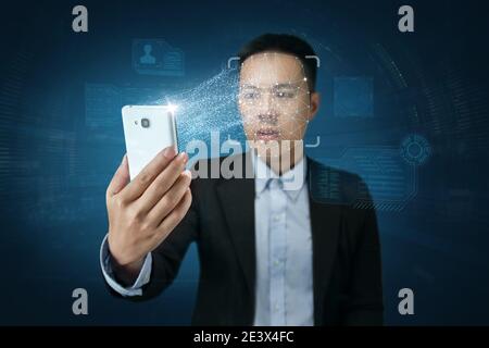 Jeune homme moderne en costume utilisant la reconnaissance faciale avec smartphone Banque D'Images