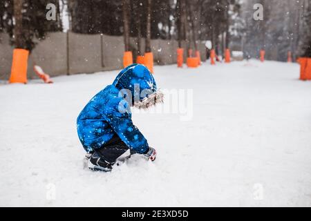 Un garçon enfant en hiver dans le parc sculpte un bonhomme de neige de la neige Banque D'Images