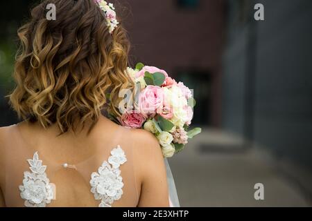 Arrière de la mariée dans une robe de mariage blanche gros plan. Bouquet de roses de mariée dans des couleurs pastel, boucles. Ailes d'ange dans la décoration de la robe. BRI Banque D'Images