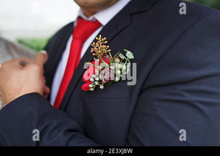 La boutonnière de mariage du marié est une veste noire avec une cravate rouge. Elle est agrémentée de succulents et de fleurs rouges. Décoration festive, fleurs, tenue pour le régist de mariage Banque D'Images