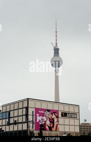 Berlin, Allemagne - 30 juillet 2019: Saturn avec deux filles embrassant sur panneau d'affichage dans Karl-Marx-Allee contre la tour des télécommunications un jour farade Banque D'Images