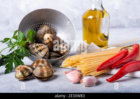 sur fond gris, dans une vieille passoire, des palourdes fraîches à la carapace, des spaghetti et divers ingrédients pour la préparation des pâtes. Toujours Banque D'Images