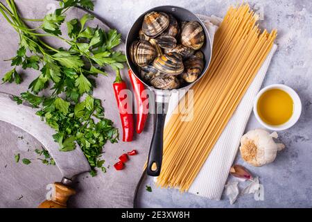 sur fond gris, dans une vieille passoire, des palourdes fraîches à la carapace, des spaghetti et divers ingrédients pour la préparation des pâtes. Toujours Banque D'Images