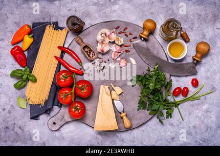 Cuisine italienne : sur une planche à découper en bois gris, spaghetti crus, fromage vieilli, nombreux ingrédients et herbes aromatiques, un couteau en croissant. Vue de l'abov Banque D'Images