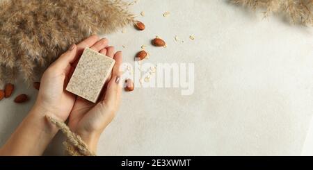 Mains féminines tenant une savon fait main sur un fond beige décoré avec des amandes, un cadeau de savon naturel pour le soin personnel Banque D'Images