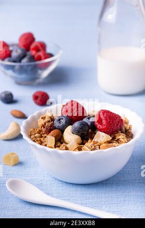 sur table bleu lavande, petit-déjeuner avec lait frais, dans un bol de mélange de fruits secs, de grains entiers, de gingembre confit, de bleuets et de framboises Banque D'Images