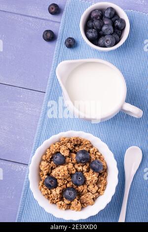 sur table bleu lavande, petit déjeuner sain avec muesli croquant d'orge et d'avoine, myrtilles et lait frais. Vue de dessus. Banque D'Images