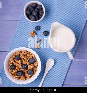 sur table bleu lavande, petit déjeuner sain avec muesli croquant d'orge et d'avoine, myrtilles et lait frais. Vue de dessus. Banque D'Images