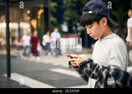 enfant asiatique adolescent regardant le téléphone portable tout en marchant dans la rue Banque D'Images