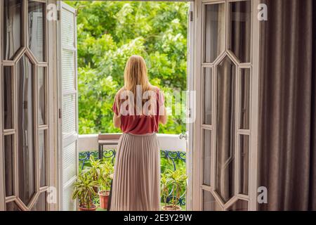 Une femme aux cheveux de gingembre se tient sur un balcon de style ancien en dégustant son café du matin. Une femme dans un hôtel en Europe ou en Asie comme tourisme récupère d'un Banque D'Images