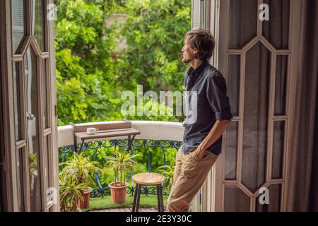 l'homme se tient sur un balcon de style ancien en dégustant son café du matin. Un homme dans un hôtel en Europe ou en Asie comme tourisme se remet d'une pandémie. Tourisme Banque D'Images