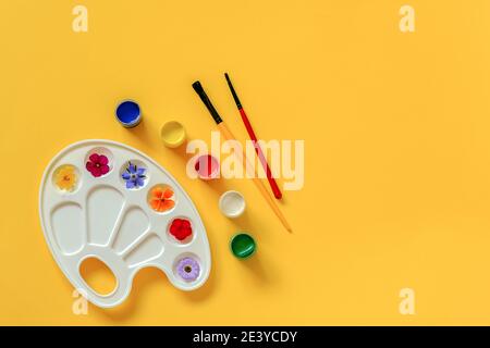 Fleurs colorées sur palette artistique, pinceau, gouache sur fond jaune, espace de copie. Concept créatif couleurs d'été ou Journée internationale des fleurs. Haut Banque D'Images
