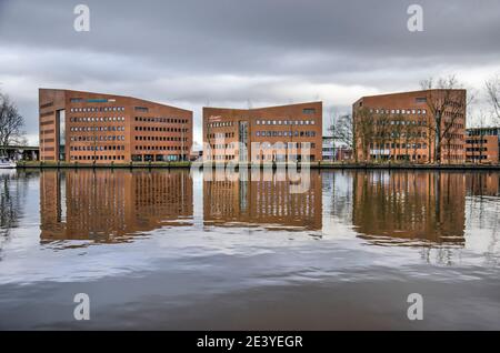 Gouda, pays-Bas, 30 décembre 2020 : trois bâtiments scolaires et de bureaux en briques se reflétant dans le fleuve Gouwe sous un ciel nuageux Banque D'Images