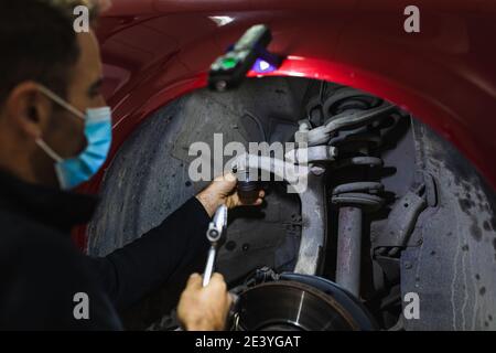 mécanicien répare la suspension de voiture. Concentrez-vous sur les mains. COVID 19 Banque D'Images