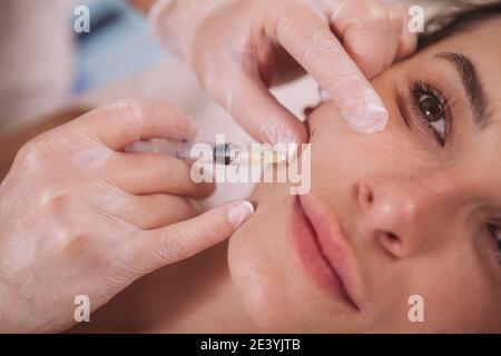 Courte vue rapprochée d'une belle femme qui obtient des injections de remplissage dans son visage. Jeune femme recevant des injections d'acide hyaluronique par le cosmetologiste Banque D'Images