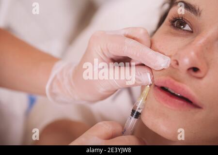 Petit gros plan d'une belle jeune femme qui reçoit des injections de lèvres par un cosmetologiste professionnel. Une cliente féminine obtient une procédure d'augmentation de la lèvre à Banque D'Images