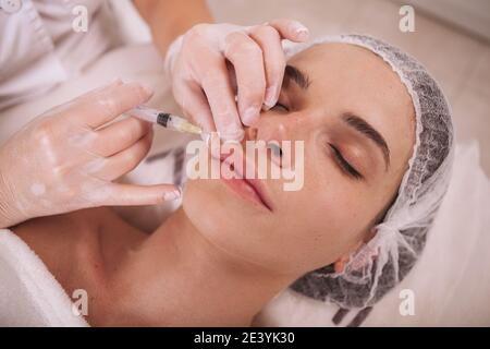 Jeune femme qui obtient des injections d'augmentation de lèvre par un cosmetologiste professionnel. Esthéticienne injectant du mastic dans les lèvres de la cliente femelle Banque D'Images