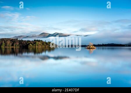 Ciel bleu, lumière du soleil dorée sur une petite île et inversion de nuages sous Skiddaw. Tout se reflète dans un Derwentwater calme, Lake District, Angleterre. Banque D'Images