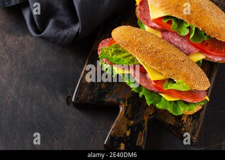 Des sandwiches sains avec du pain de son, du fromage, de la laitue verte, de la tomate et des tranches de salami sur un support en bois rustique. Concept petit déjeuner. Vue de dessus. Banque D'Images