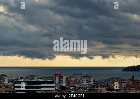 Paysage spectaculaire de ciel orageux au-dessus de la petite ville côtière. Le ciel est devenu jaune avant la tempête. Des nuages nimbostratus sombres s'accrochent au-dessus de la ville et de la mer. Banque D'Images