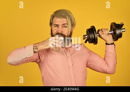 Exercice dans la salle de sport. Lait bons nutriments. Quantité de graisse. Vitamines pour les muscles. Le sportif tient un haltère et un verre de lait. Régime protéique. Cocktail de protéines. Source de calcium. L'homme barbu boit du lait. Banque D'Images