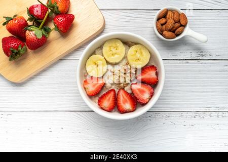 Porridge de flocons d'avoine avec fraises, amandes et banane dans un bol blanc. Un petit déjeuner sain avec des flocons d'avoine et de la fraise biologique fraîche. Nourriture végétalienne. Saine Banque D'Images