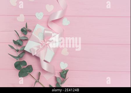 Cadeau de Saint-Valentin ou de mariage, feuilles d'eucalyptus cadre papier coeurs confetti et bois rose fond, espace vide pour votre texte, vue de dessus plat Banque D'Images