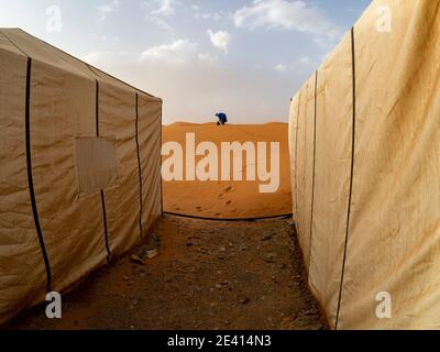 Un homme en vêtement berbère bleu, entre deux tentes établies dans le désert marocain du Sahara. Banque D'Images