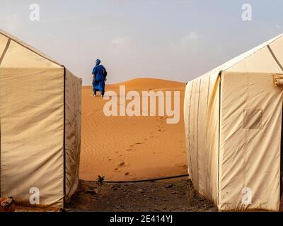 Un homme en vêtement berbère bleu, entre deux tentes établies dans le désert marocain du Sahara. Banque D'Images