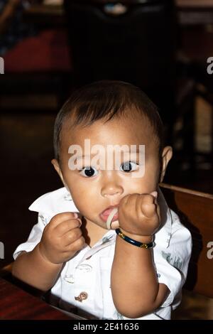 Bébé philippin américain fasciné par les nouilles Udon pendant qu'il est assis dans sa chaise haute, les yeux sont larges Banque D'Images