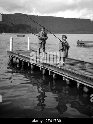 Un garçon et une fille, peut-être frère et sœur, pêchent dans un lac au large d'une promenade, dans les années 1940 ou 1950 Banque D'Images