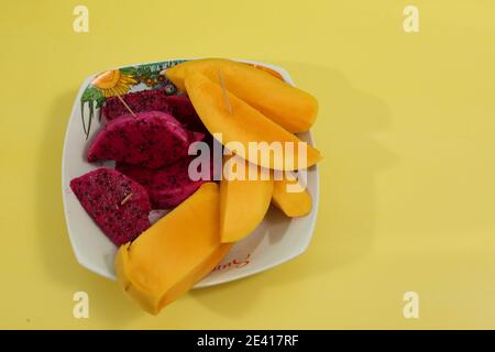 Vue de dessus d'un plat de mangue fraîche mûre et tranches de fruits dragon isolées sur fond jaune Banque D'Images