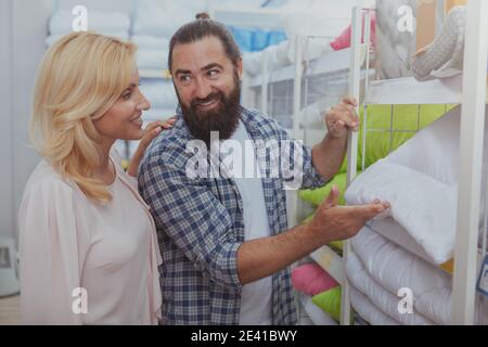 Joyeux barbu homme choisissant des oreillers orthopédiques au grand magasin, shopping avec sa belle femme. Couple achetant des biens pour leur nouvelle maison Banque D'Images