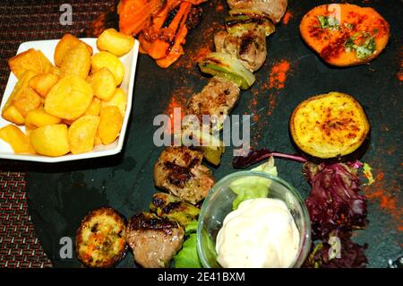 Cuisine catalane colorée. Kebab avec pommes de terre cuites au four et légumes grillés (aubergine, patate douce, poivron rouge, etc.) et salade fraîche servie sur plaque de pierre Banque D'Images