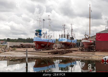 Bonnerup, Danemark - 15 juillet 2020 : les coupeurs de pêche bleus sont dans le quai et sont en cours de réparation, tous deux reflétés dans l'eau, des nuages spectaculaires dans le ciel Banque D'Images