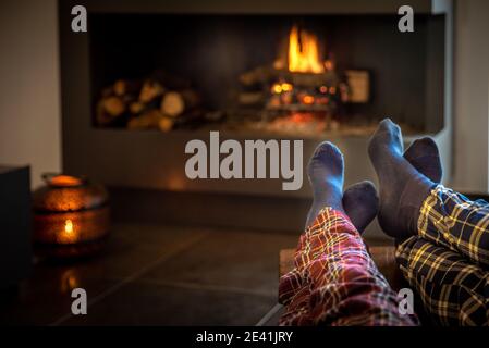 Le couple assis devant la cheminée se détend avec le feu chaud en réchauffant ses pieds. Concept des vacances d'hiver, des vacances de noël et de l'amour Banque D'Images