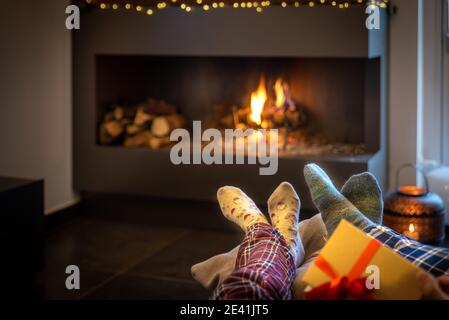 Le couple assis devant la cheminée se détend avec le feu chaud en réchauffant ses pieds. Concept des vacances d'hiver, des vacances de noël et de l'amour Banque D'Images