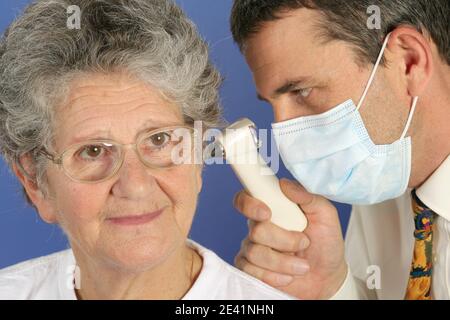 Le médecin avec un masque examine l'oreille du patient avec un otoscope. La patiente est une femme de plus de 70 ans Banque D'Images