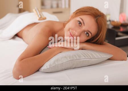 Joyeuse belle femme souriante joyeusement, couchée sur une table de massage au spa. Détente, rajeunissement, concept de mode de vie sain Banque D'Images