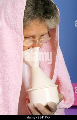 femme de 65 ans avec une serviette au-dessus de la tête inhalant essentiel vapeur d'huile comme traitement alternatif Banque D'Images