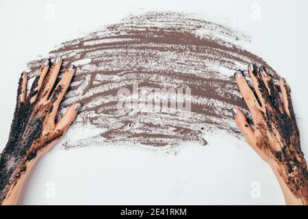 Mains de femmes avec masque cosmétique appliqué poudre d'argile noire pulvérisée sur la table, vue de dessus. Banque D'Images