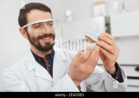 Accent sélectif sur la moisissure dentaire dans les mains de dentiste masculin gai. Beau technicien dentaire tenant des prothèses dentaires Banque D'Images