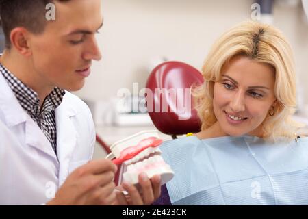 Male dentist montrant sa femme comment brosser les dents correctement, l'utilisation du moule. Femme mature en regardant son dentiste expliquant à propos de dents et Banque D'Images