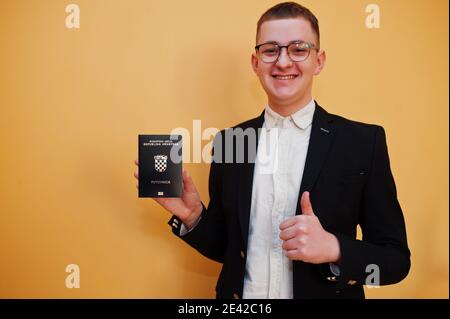 Jeune homme beau tenant la République de Croatie passeport ID sur fond jaune, heureux et montrer pouce vers le haut. Concept pays Voyage en Europe. Banque D'Images