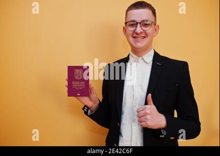 Jeune homme beau tenant la République de Finlande passeport ID sur fond jaune, heureux et montrer le pouce vers le haut. Concept pays Voyage en Europe. Banque D'Images