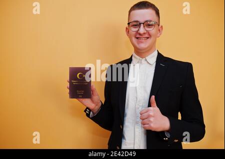 Jeune homme beau tenant la République de Turquie passeport ID sur fond jaune, heureux et montrer pouce vers le haut. Concept pays Voyage en Europe. Banque D'Images