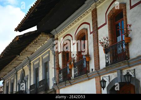 Façade de maison coloniale avec fenêtres en briques sur un mur en stuc blanc lavé avec des balustrades de balcon en fer artisanal à Zacatlán de las manzanas, Mexique. Banque D'Images