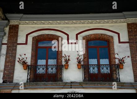 Façade de maison coloniale avec fenêtres en briques sur un mur en stuc blanc lavé avec des balustrades de balcon en fer artisanal à Zacatlán de las manzanas, Mexique. Banque D'Images