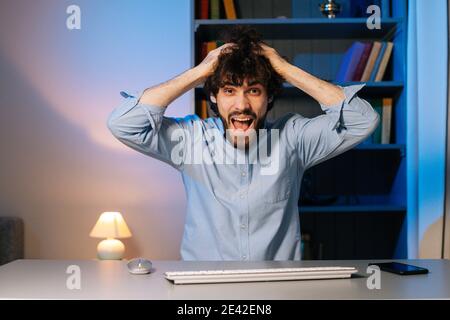 Vue avant d'un jeune homme fou tirant les cheveux sur la tête bureau avec ordinateur à la maison Banque D'Images