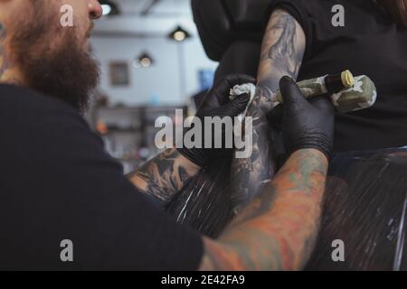 Prise de vue courte d'une femme méconnaissable dont le bras est tatoué par un tatoueur professionnel. Tatouage barbu artiste travaillant à son salon, tatouant jeune W Banque D'Images